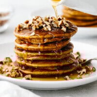 A stack of paleo pumpkin pancakes topped with pecans and maple ginger syrup.