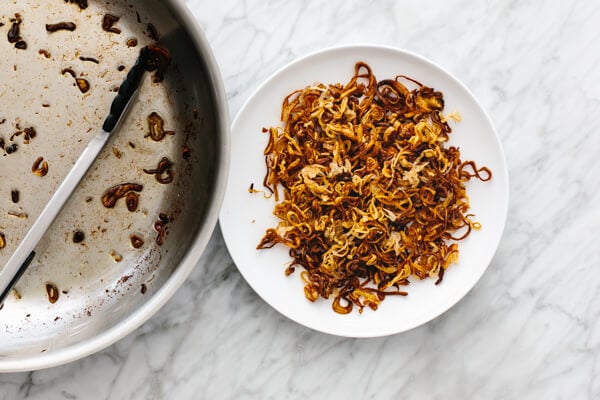 Crispy shallots on a plate next to a pan.