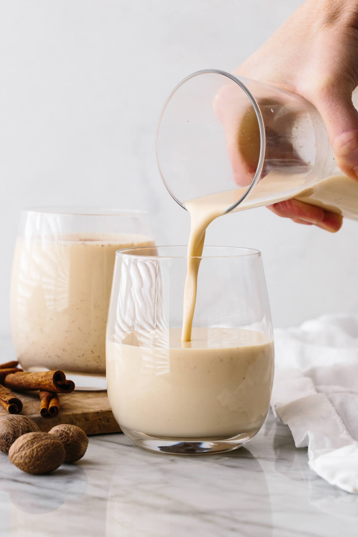Pouring eggnog into a glass on a table.