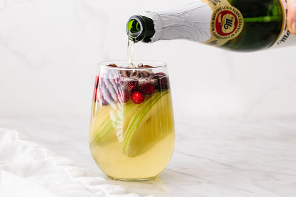 Pouring apple cider into a glass of white Christmas sangria.