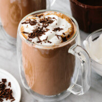 A glass of Nutella hot chocolate next to whipped cream.