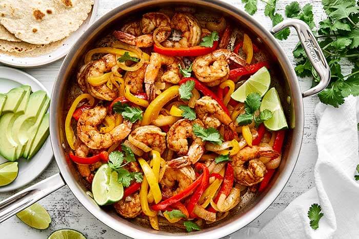Shrimp fajitas in a skillet with limes.