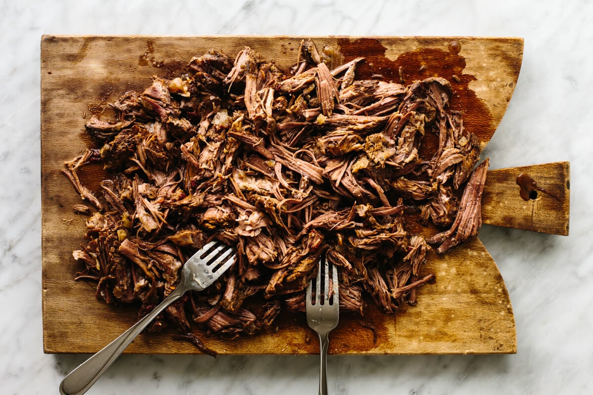 Mexican beef barbacoa that's juicy, meltingly tender, seasoned with flavorful chilies and spices, and made easy right in the slow cooker! Shredded beef barbacoa on a wooden board with forks.