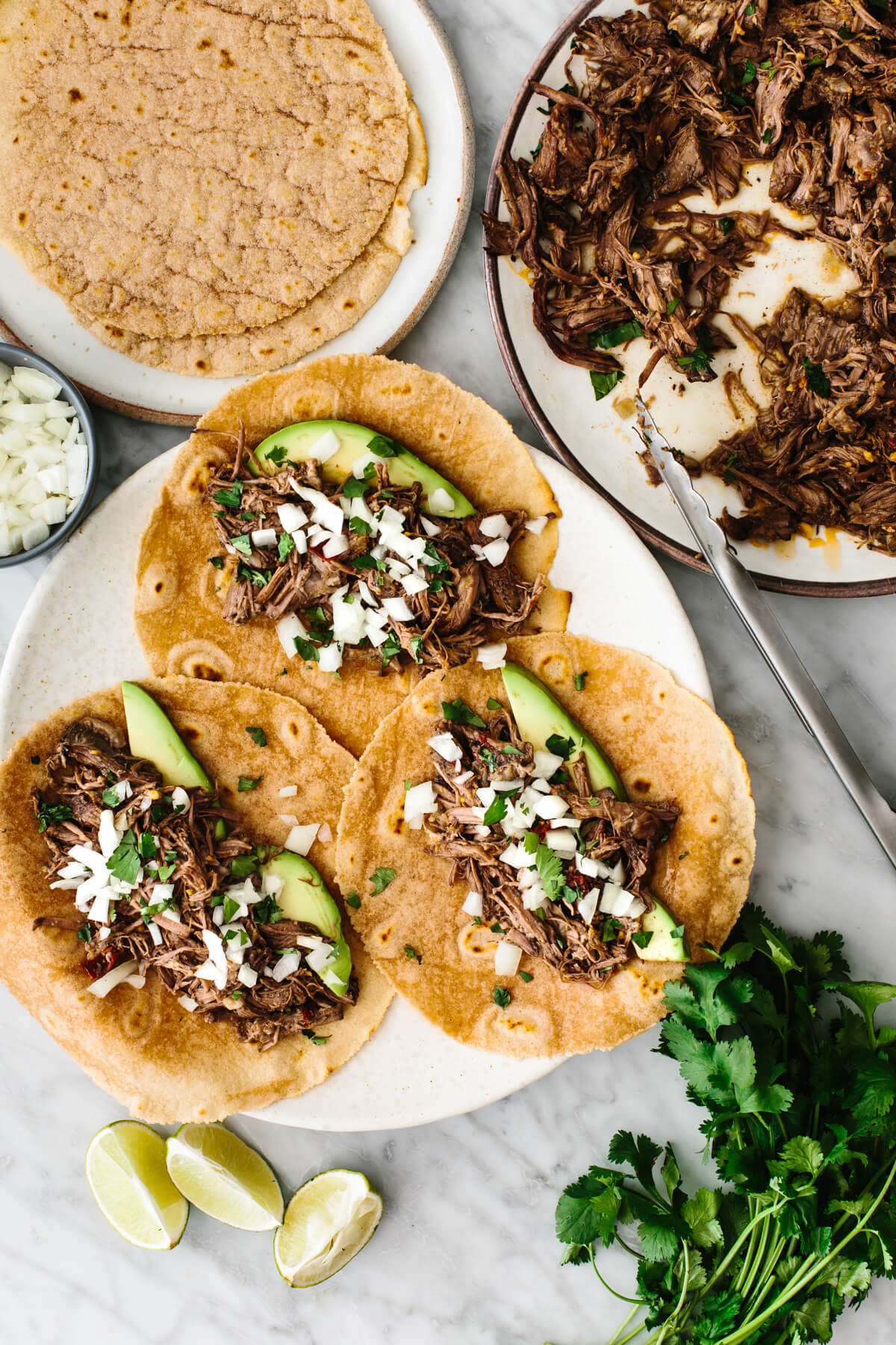 Assembling beef barbacoa tacos with tortillas.