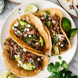 Barbacoa tacos on a plate with cilantro and lime wedges.
