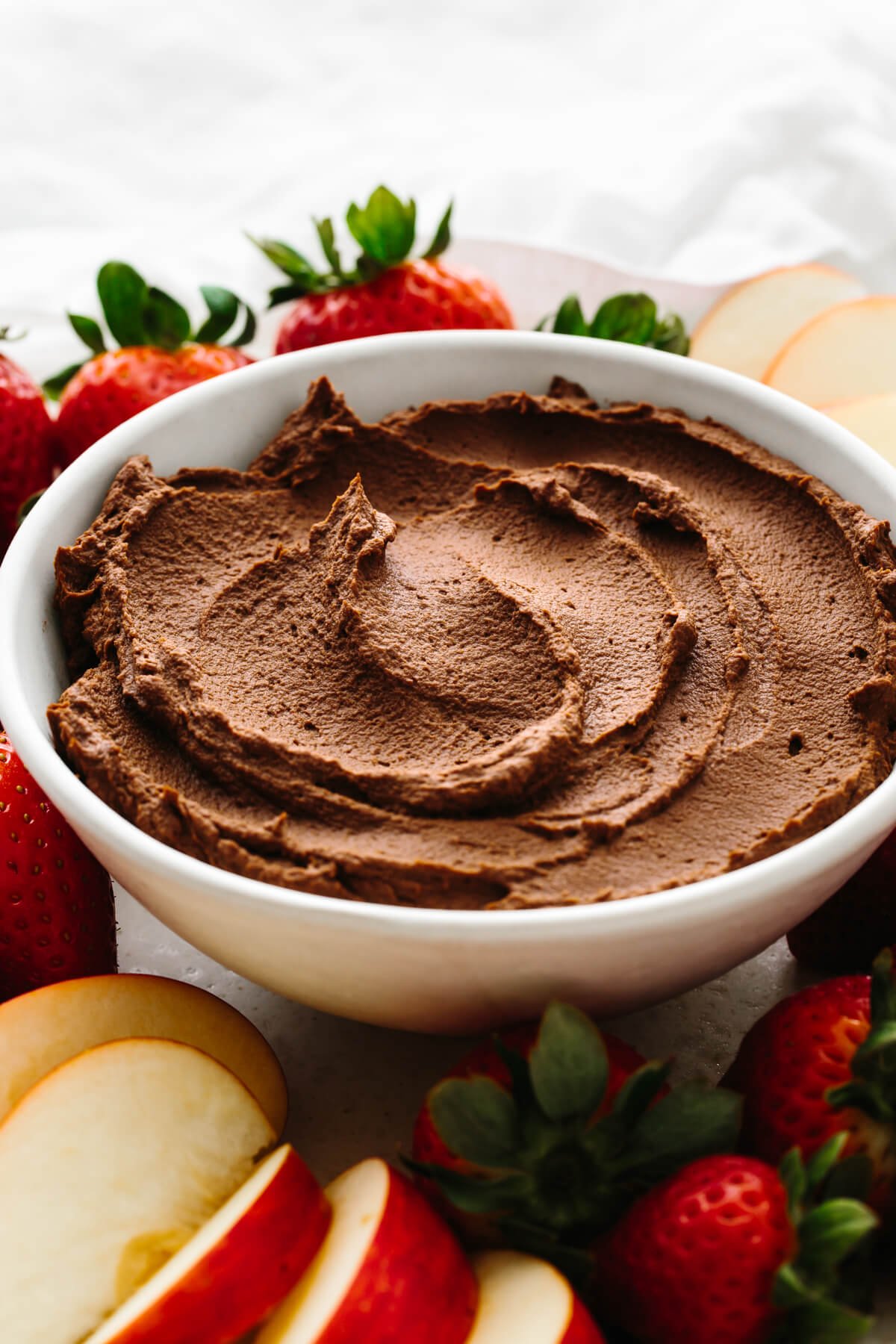A bowl of chocolate hummus next to fruits.