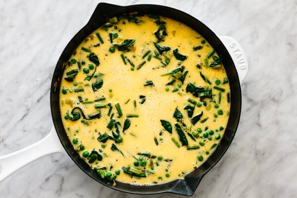 Cooking eggs with vegetables in a pan for a spring frittata