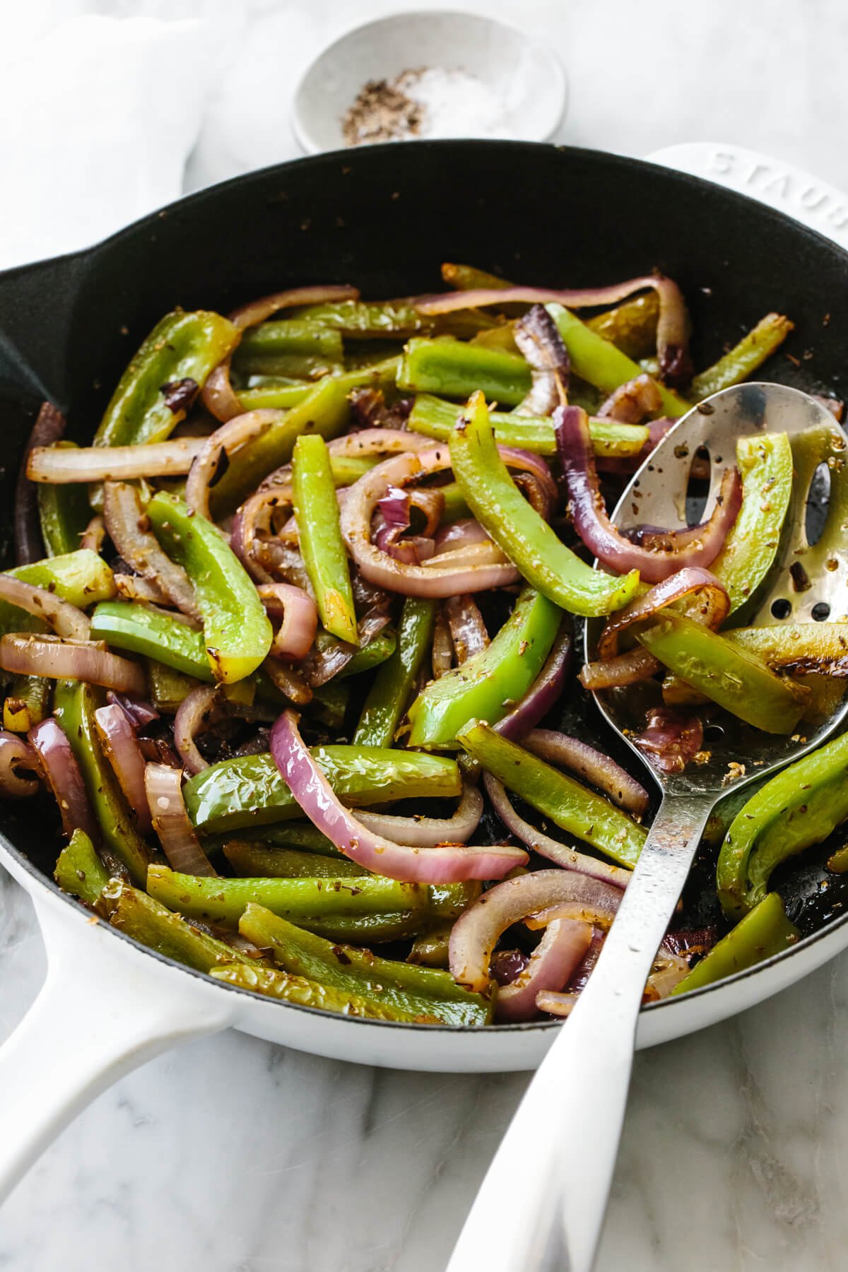 Fajita veggies in a skillet with a slotted spoon.