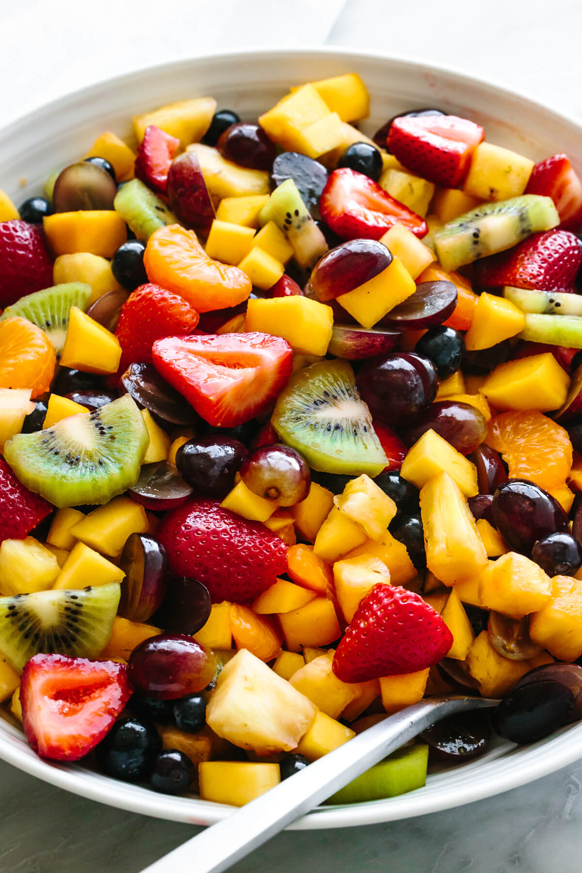 This summertime classic fruit salad is a simple combo of juicy seasonal fruit drizzled with a bright honey lime dressing. A must-have for picnics and beach days! A large bowl of fruit salad with a spoon.