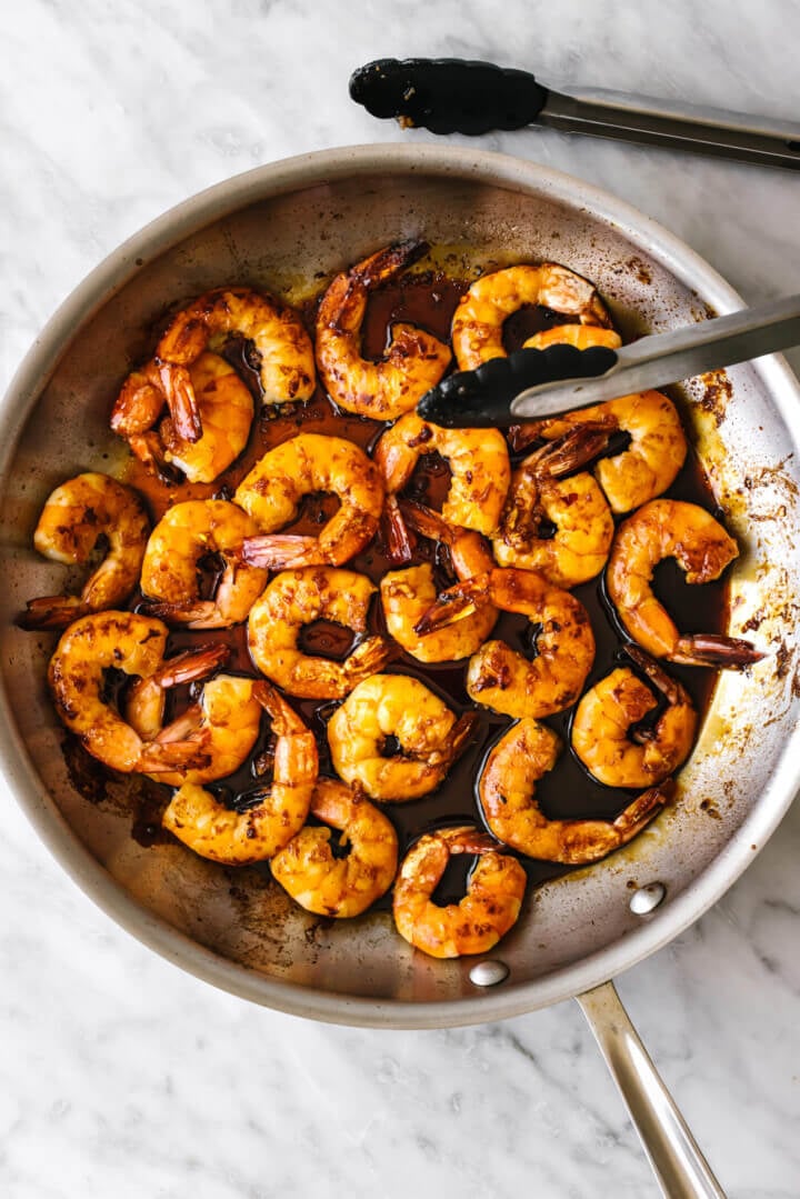 Cooking honey garlic shrimp in a metal pan with tongs