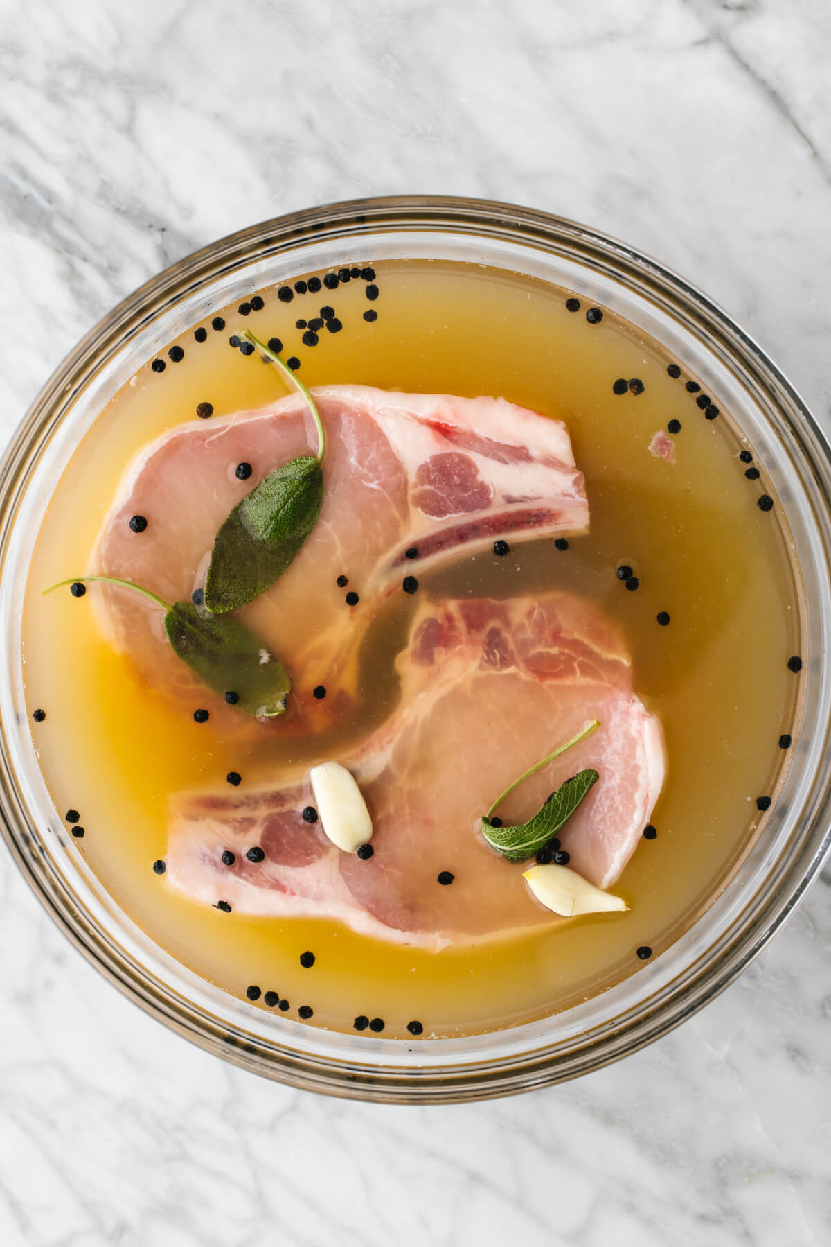 Brining pork chops in apple cider solution in a glass bowl.