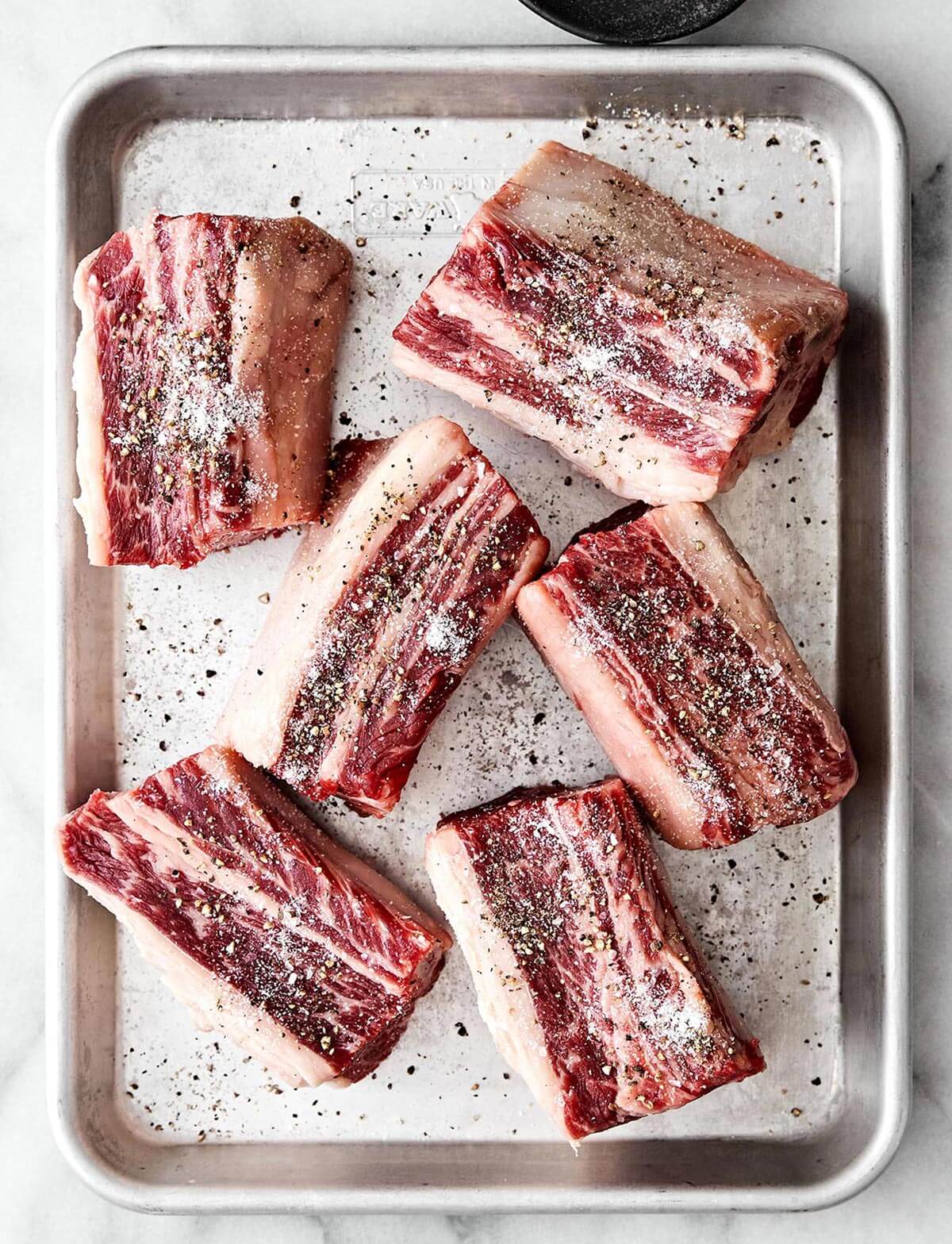 Salting short ribs on a sheet pan.