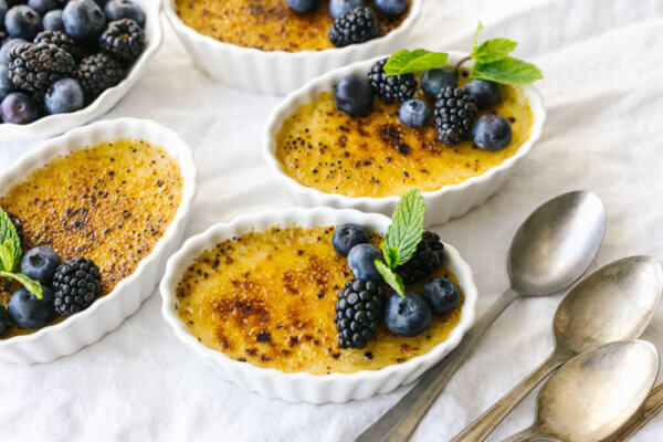 Coconut crème brûlées on a table next to berries.