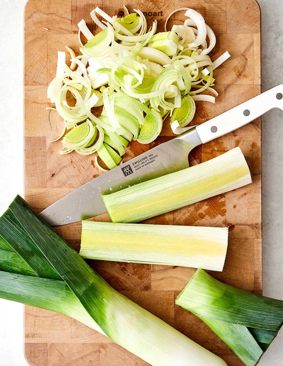 This potato leek soup is the ultimate fall soup! It's ultra-creamy, loaded with veggies, and completely vegetarian. Slicing leeks on a board.