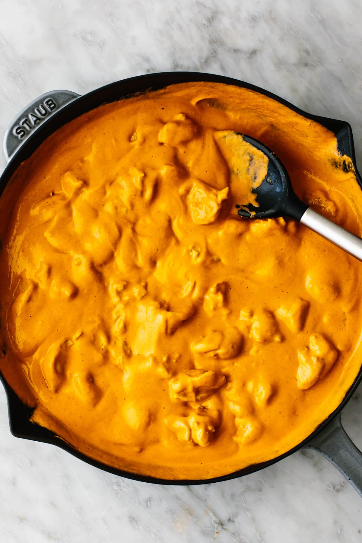 Butter chicken in a large pan with a spoon.