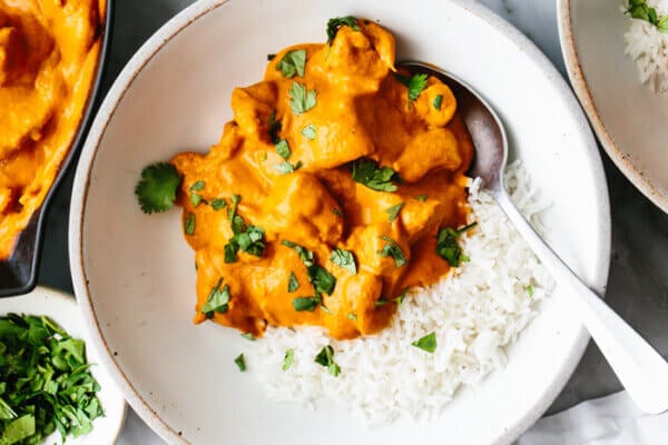 A bowl with butter chicken and rice next to cilantro