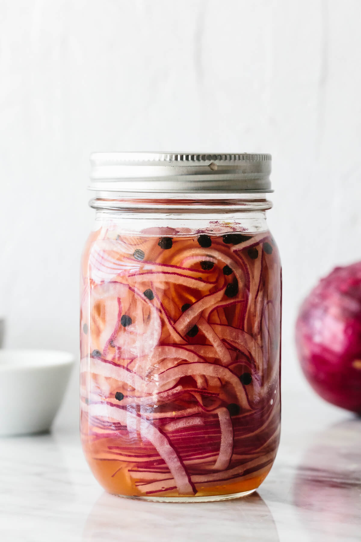 A jar of pickled red onions next to a red onion