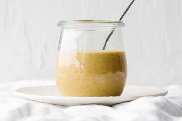 A glass jar of maple mustard tahini dressing on a plate