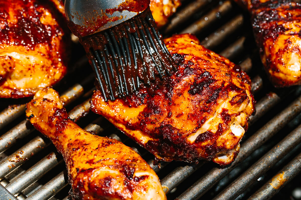 This BBQ chicken is insanely juicy, perfectly charred, and glistening with my secret homemade BBQ sauce. Perfect for your summer cookout! Brushing BBQ sauce on BBQ chicken