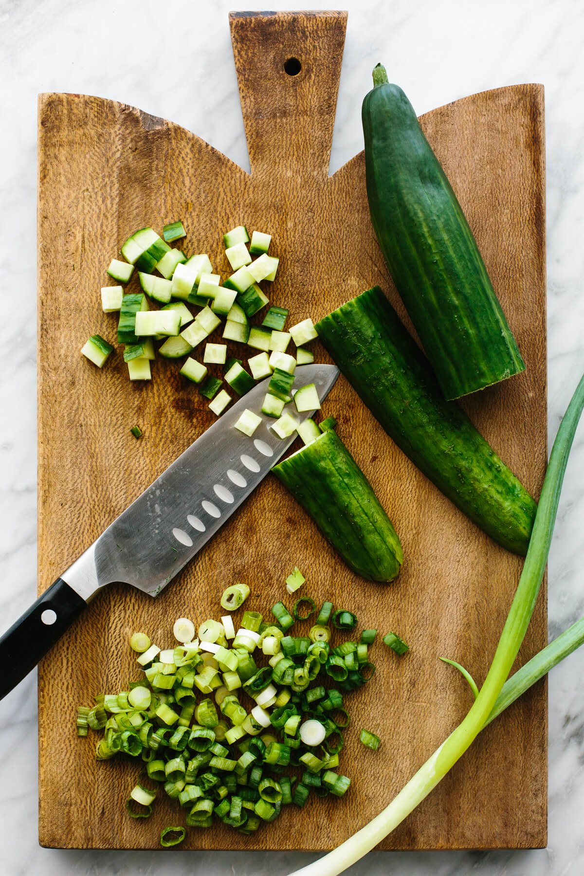 This healthy cucumber shrimp salad recipe is going to be your new favorite way to cook shrimp! Diced cold shrimp gets tossed with cucumbers, green onion, herbs, and a creamy lime dressing for the best easy dinner recipe. Diced cucumber and green onions on a board for cucumber shrimp salad