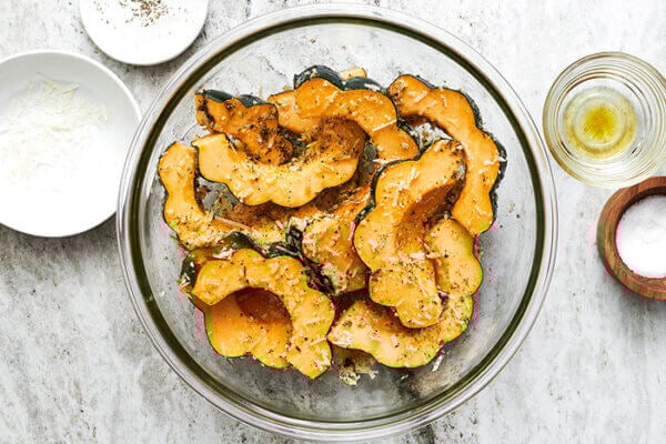 Mixing acorn squash slices with seasoning in a bowl