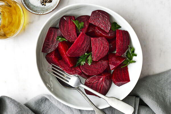 A white bowl of roasted beets next to a napkin