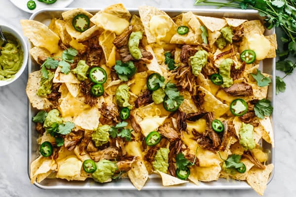 Carnitas nachos layered on a sheet pan