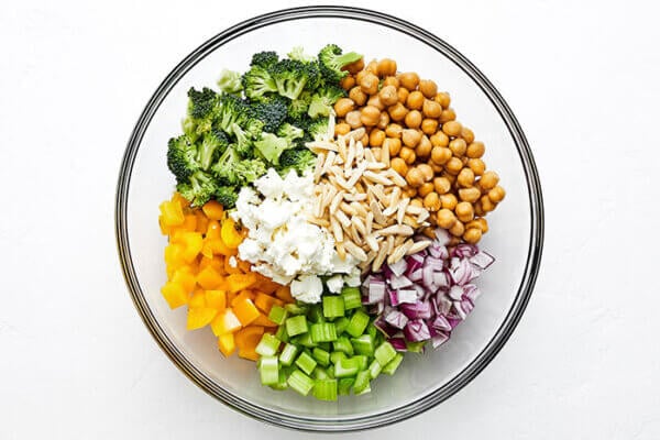 A glass bowl of chopped broccoli and chickpea salad ingredients