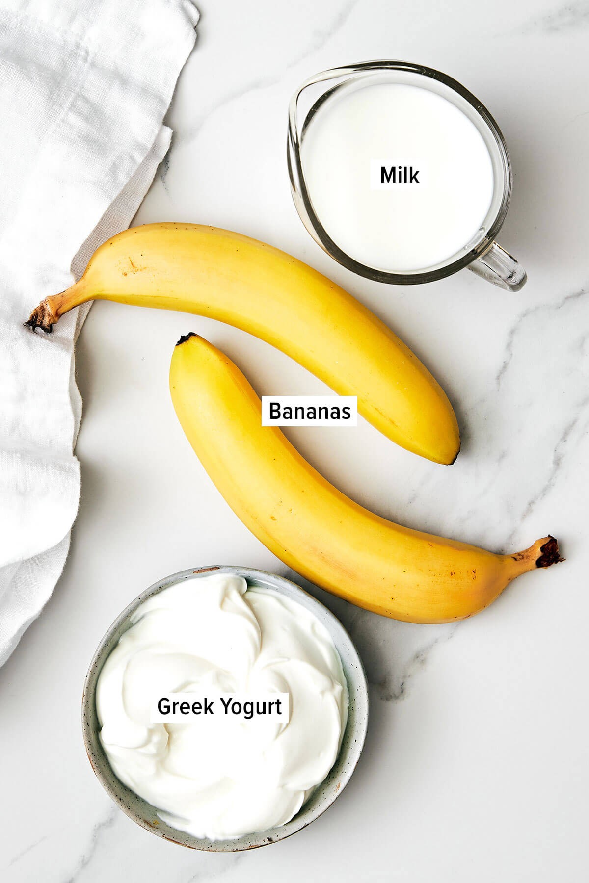 My favorite 3-ingredient banana smoothie recipe! It's simple yet tasty with frozen bananas, a milk of your choice, and Greek yogurt. Ingredients for banana smoothie on a table