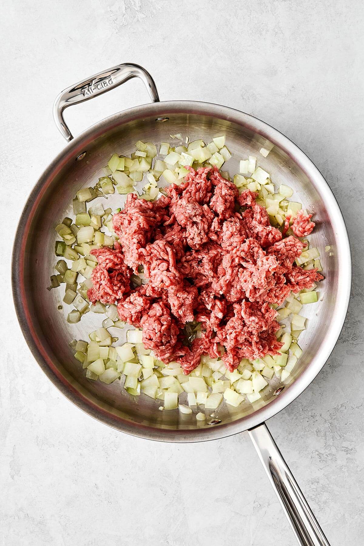 Stuffed peppers are always a family favorite weeknight dinner. This classic version is packed with the best filling — juicy ground beef, fluffy rice, and plenty of veggies seasoned with Italian flavors. Cooking ground beef and onion in a pan.