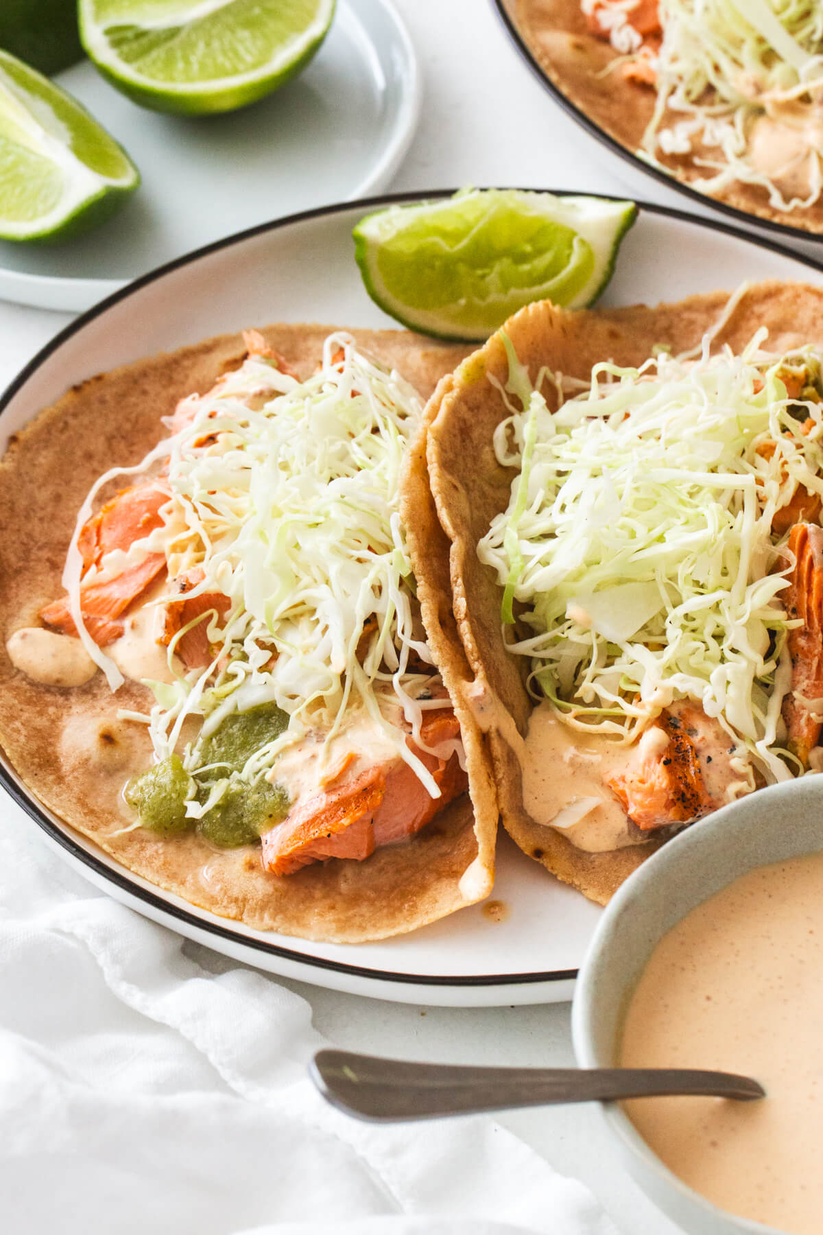 These Baja grilled salmon tacos are the best easy dinner with homemade salsa verde, creamy chipotle sauce, shredded cabbage, and cilantro. Close up of salmon tacos
