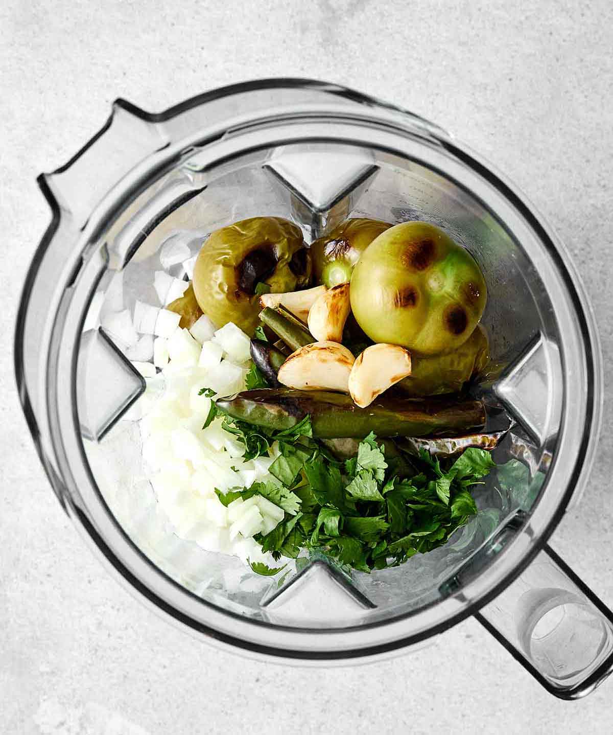 Adding roasted salsa verde ingredients into a blender.