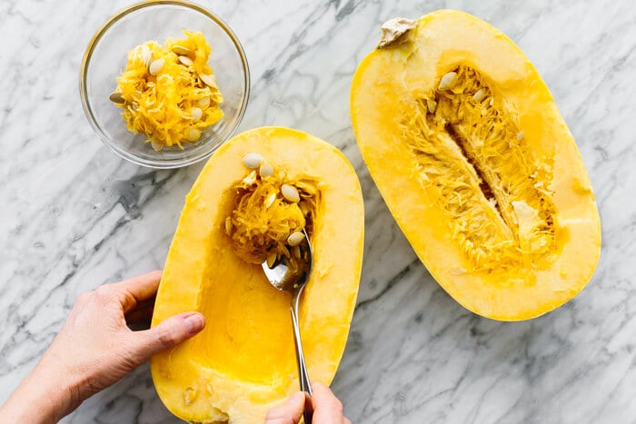 Scraping the seeds out of a spaghetti squash.