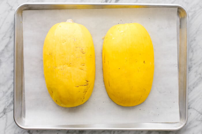 Two halves of spaghetti squash on a baking sheet.