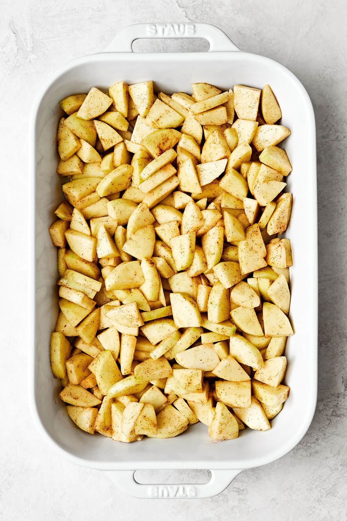 This apple crisp is the best holiday dessert with a sweet cinnamon apple filling and oat crumble topping — especially during Thanksgiving! Prepping apples in a casserole dish.