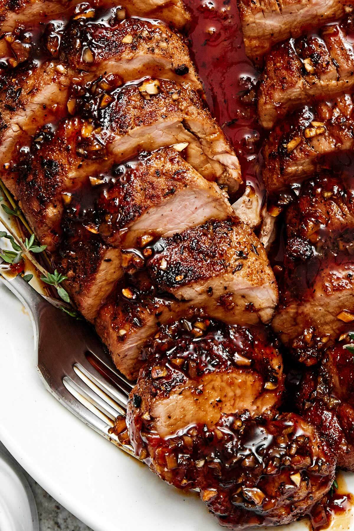 The juiciest pork tenderloin that's seasoned with a flavorful spice blend, seared to a golden crust, and baked with the best honey garlic sauce. Sliced pork tenderloin with sauce.