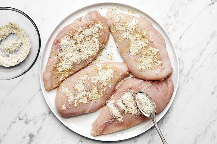 Coating chicken breasts with lemon pepper seasoning.