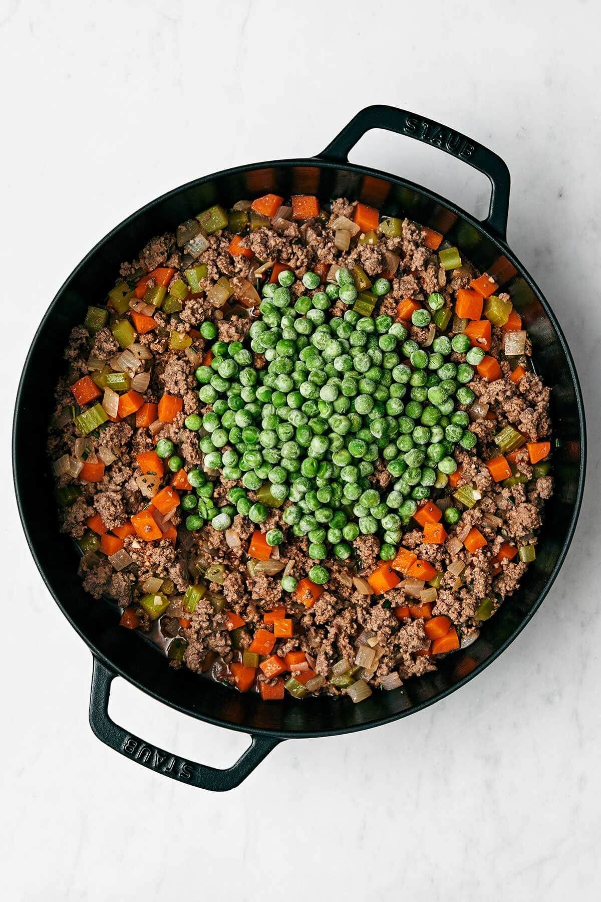 Cooked cottage pie filling with peas in a pan.