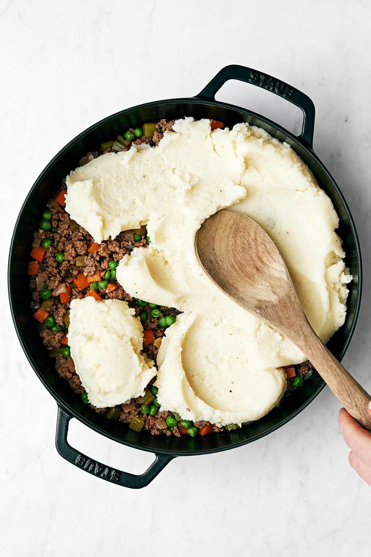 Adding mashed potatoes on top of cottage pie.