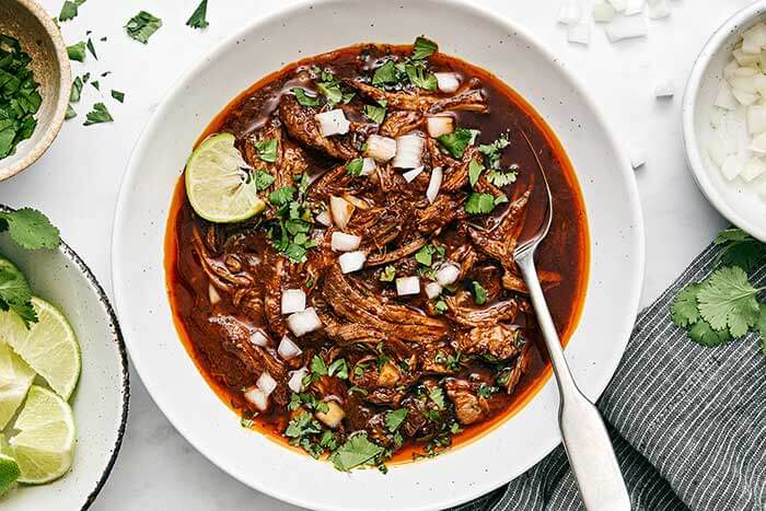 A bowl of birria de res with a lime.