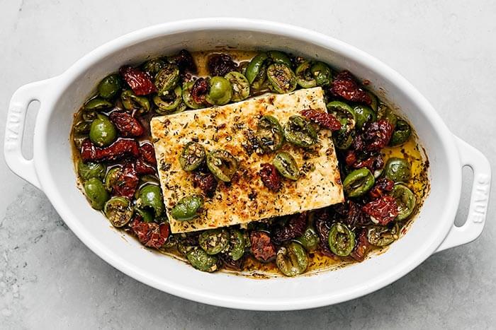 A baking dish with feta cheese, olives, and sun-dried tomatoes.