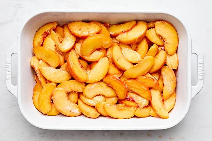 Sweet peach crisp filling in a casserole dish.