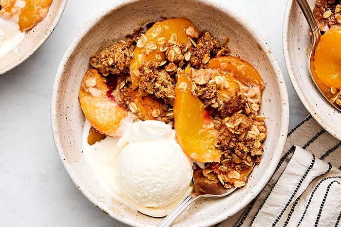 Peach crisp in a bowl with ice cream on top.