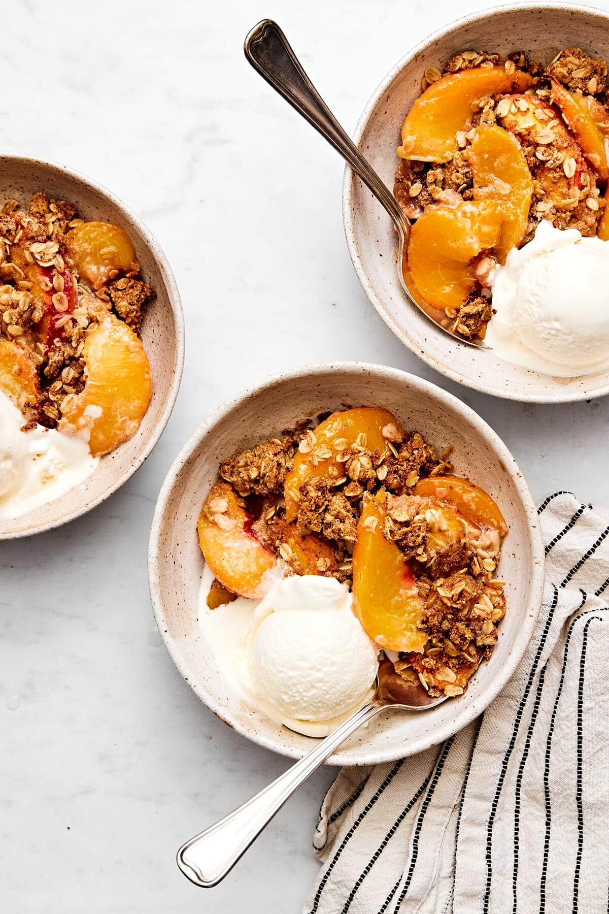 This peach crisp dessert with a crumble oatmeal topping is the best way to celebrate summer peach season! Plus, it's completely gluten-free. Peach crisp in bowls with ice cream.