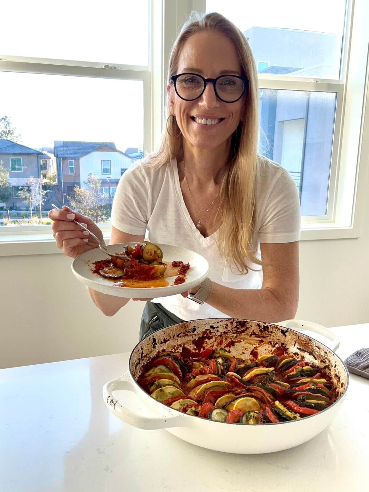 Lisa holding a plate of ratatouille next to the pan.