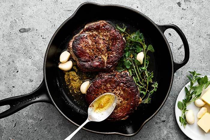 Cooking ribeye steaks in a cast iron pan with butter.