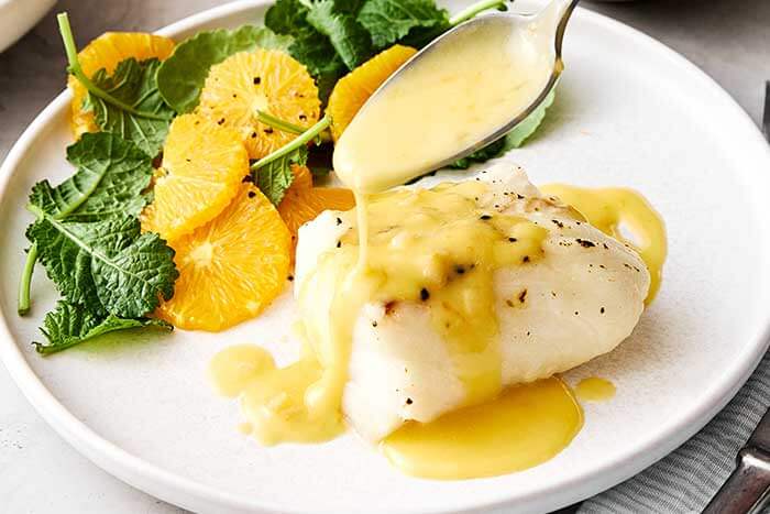 Drizzling orange beurre blanc on baked cod.