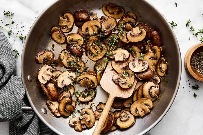 A pan with sauteed mushrooms and thyme.