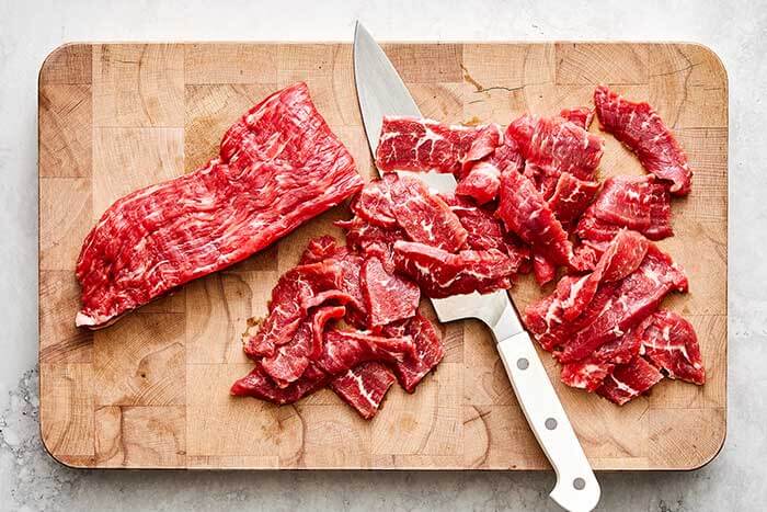 Sliced flank steak on a wooden board.
