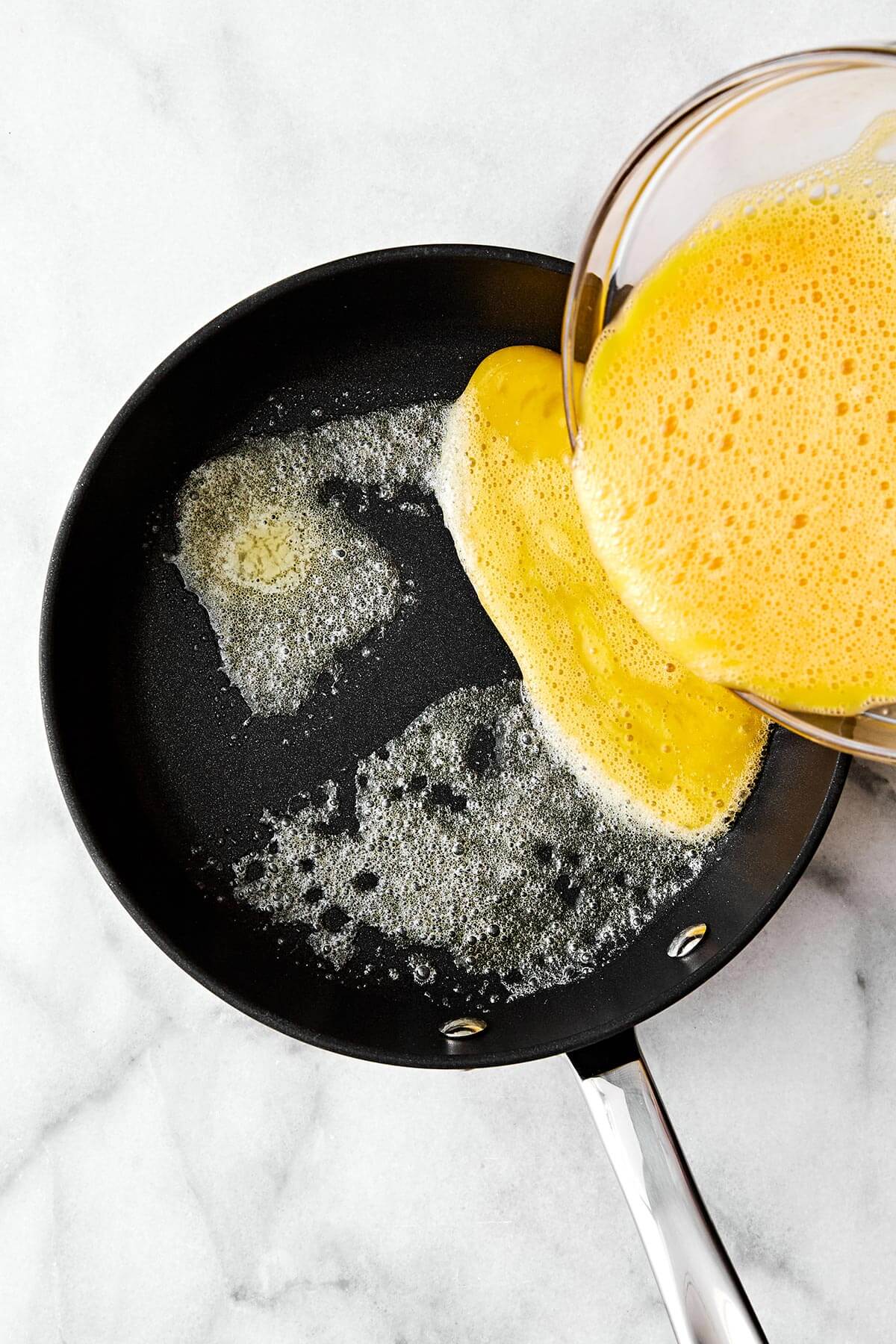 Learn how to make scrambled eggs with my easy, foolproof method! Your eggs will turn out silky and creamy every single time. Adding whisked eggs into a pan.